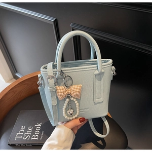 Hellblaue Eimertasche mit Lychee-Muster und Perlen-Schleife auf einem Holzstuhl