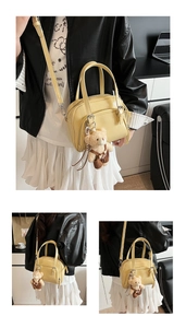 Detail of yellow faux leather boston bag featuring a teddy bear charm and zippered front