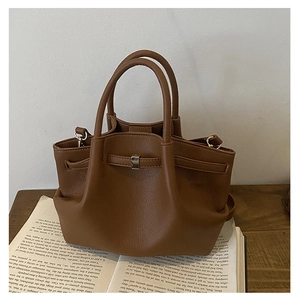 Detail of dark brown pleated bucket bag with lychee grain texture on a book