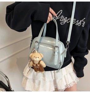 Light blue faux leather handbag shown on model featuring double zipper and bear charm
