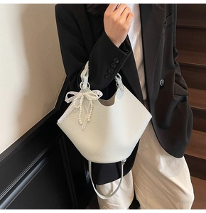 Close-up of a white lychee leather bucket bag with lace bow and pearl charms for women