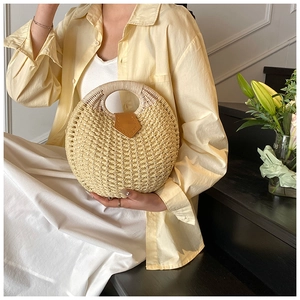 Detail of a round woven straw handbag featuring a brown leather decorative buckle
