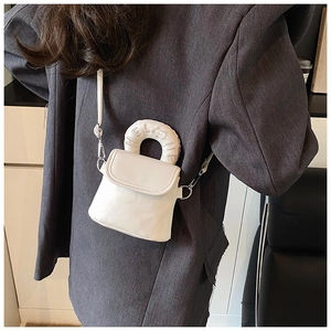 Detail showing white mini crossbody bag with embroidered bear handle on grey blazer