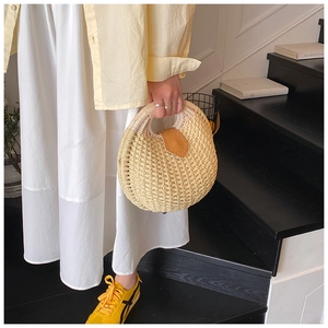 Detail of semicircular straw handbag with brown leather lid held by a model in a French style