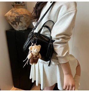 Detail of a shiny black oil wax leather crossbody bag with a cute teddy bear charm