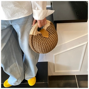 Detail of round straw handbag featuring bi-color weave and leather flap closure
