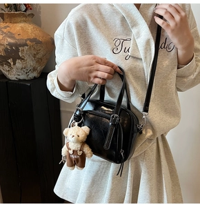 Detail of black glossy small square bag with cute white bear plush charm and dual handles