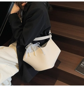 Detailed view of cream pebble leather bucket bag with elegant pearl lace bow charm