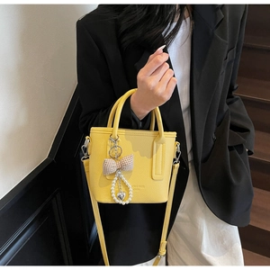 Detail der gelben Handtasche mit Litschi-Struktur, Perlen-Herzanhänger und Schleife