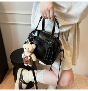 Detail of black glossy faux leather Boston bag with a cute plush bear charm