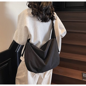 Detail of a large black minimalist slouchy tote bag worn cross-body on a wide strap