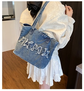 Detail van de grote blauwe denim tote bag met sterpatches gedragen door een model over wit