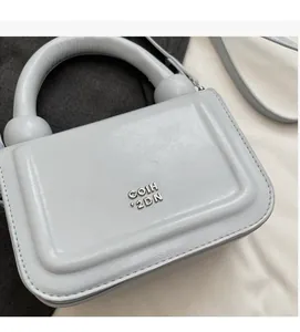 Détail d'un petit sac carré bleu-gris avec logo argenté et poignée arrondie