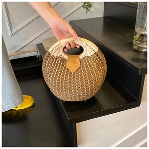 Detail of round straw bag with brown leather patch and woven texture on wooden stairs