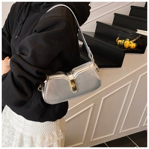 Détail du sac baguette argenté avec fermoir rotatif doré sur une bandoulière chic