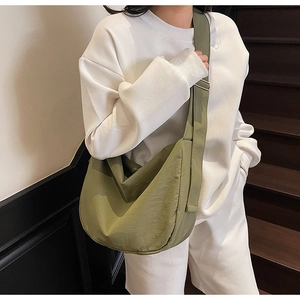 Side view of an avocado green crescent tote bag worn by a model in casual white outfit