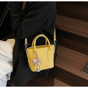 Detail der gelben Leder-Eimertasche mit Schleifenanhänger und Perlenherz-Charm