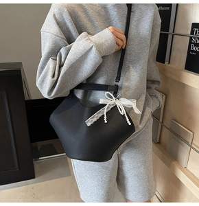 Detail of black litchi pattern leather bucket bag with white lace pearl bow decoration