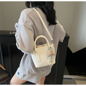 Detail einer weißen Leder-Eimertasche mit Perlenanhänger und Herzdeko an einem Model