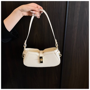 Détail d'un sac sous le bras crème avec fermoir rotatif doré sur fond de bois