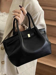 Minimalist black pebbled leather bucket bag with gold buckle on wooden stairs