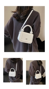 Détail du sac à main blanc structuré avec poignée cylindrique épaisse et logo gravé