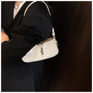 Détail d'un sac sous les aisselles en cuir verni crème avec fermoir doré sur un blazer noir