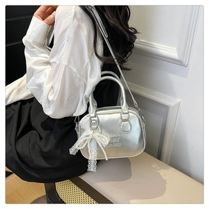 Détail du sac Boston argenté avec texte embossé et pendentif nœud en dentelle blanche