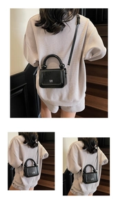 Détail d'un mini sac carré en cuir verni noir avec poignée ronde sur un escalier