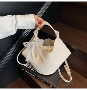 Detail of beige lychee textured bucket bag featuring lace pearl bow and drawstring liner