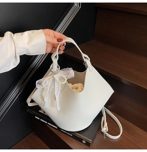 Close-up of light grey litchi texture bucket bag with pearl lace bow charm on stairs