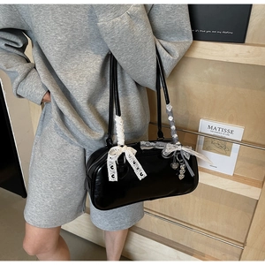 Close-up of black patent leather shoulder bag with lace bows and silver heart charms