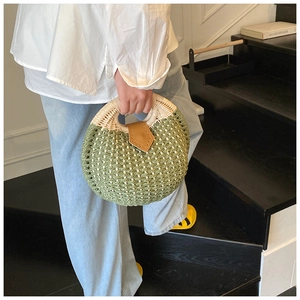 Close-up of green woven straw shell bag with brown leather clasp and round handles
