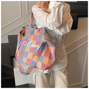 Detail of red, blue, and yellow plaid tote bag with Mearey embroidery on a model