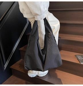 Close-up of black nylon hobo tote bag with zipper side pocket on a wooden staircase