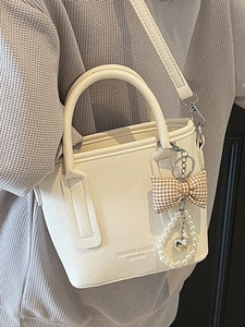 Minimalistische beigefarbene Eimertasche mit Karoschleife und Herz-Perlenanhänger