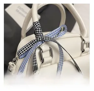 Détail d'un sac à main en cuir blanc avec un nœud en ruban à carreaux et anneaux argentés
