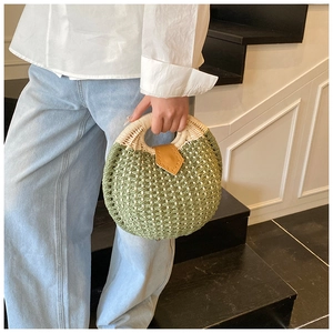 Detail of round green and beige woven straw handbag with a stylish brown leather patch
