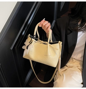 Detailed view of beige bucket bag with diamond weave texture and white mesh bow charm