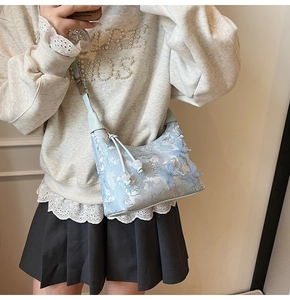 Detail of light blue satin hobo bag with white floral embroidery and 3D butterfly decor