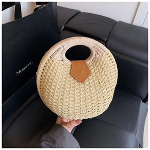 Detailed view of round straw handbag with brown leather strap on dark background