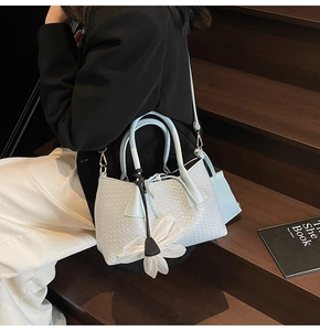 Detail of light blue woven bucket bag with floral charm and removable inner pouch