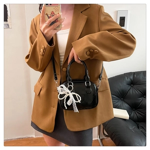 Détail du sac en cuir verni noir avec nœud en dentelle perlée et texte logo embossé