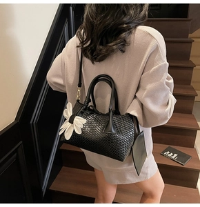 Close-up of black woven tote bag with white flower charm and detachable strap
