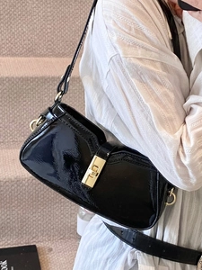 Sac sous le bras élégant en cuir verni noir avec boucle dorée porté à l'épaule
