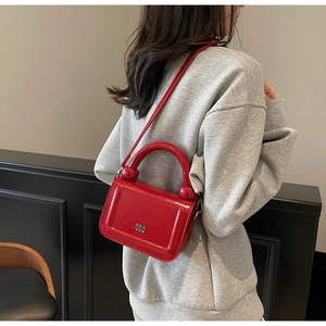 Détail du sac à main rouge brillant avec poignée cylindrique et logo argenté