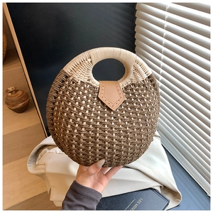 Close-up of circular straw woven bag featuring a brown leather flap and round top handle