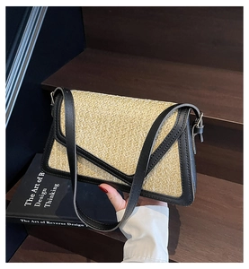 Detail of woven straw crossbody bag with black leather trim on a vintage wooden background