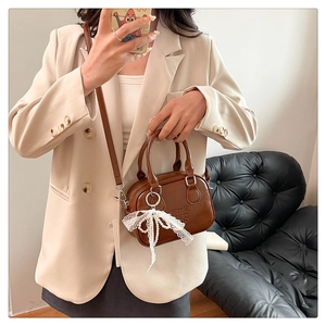 Détail du sac bowling marron avec nœud en dentelle et breloque perle sur blazer beige