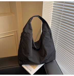 Detail of minimalist black nylon tote bag showing wrinkled texture and side zipper pockets